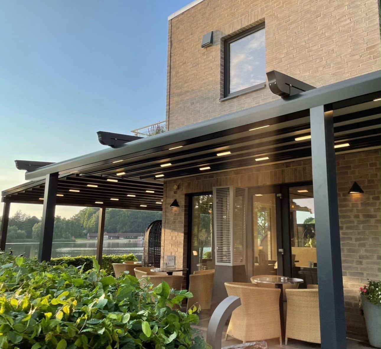 Terrassenüberdachung aus anthrazitfarbenem Aluminium an einem Klinkerhaus mit Lounge-Möbeln